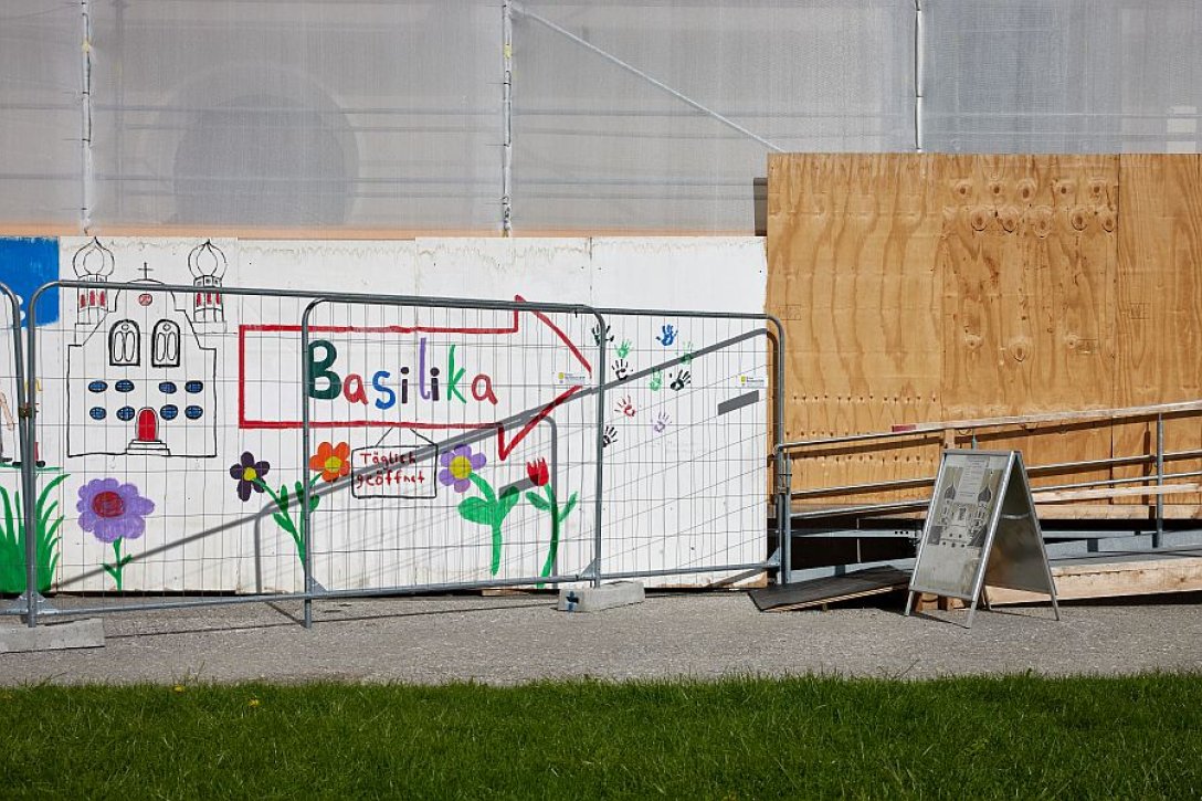 Mit bunten Farben bemalte und beschriftete Wand mit Text: Basilika täglich geöffnet