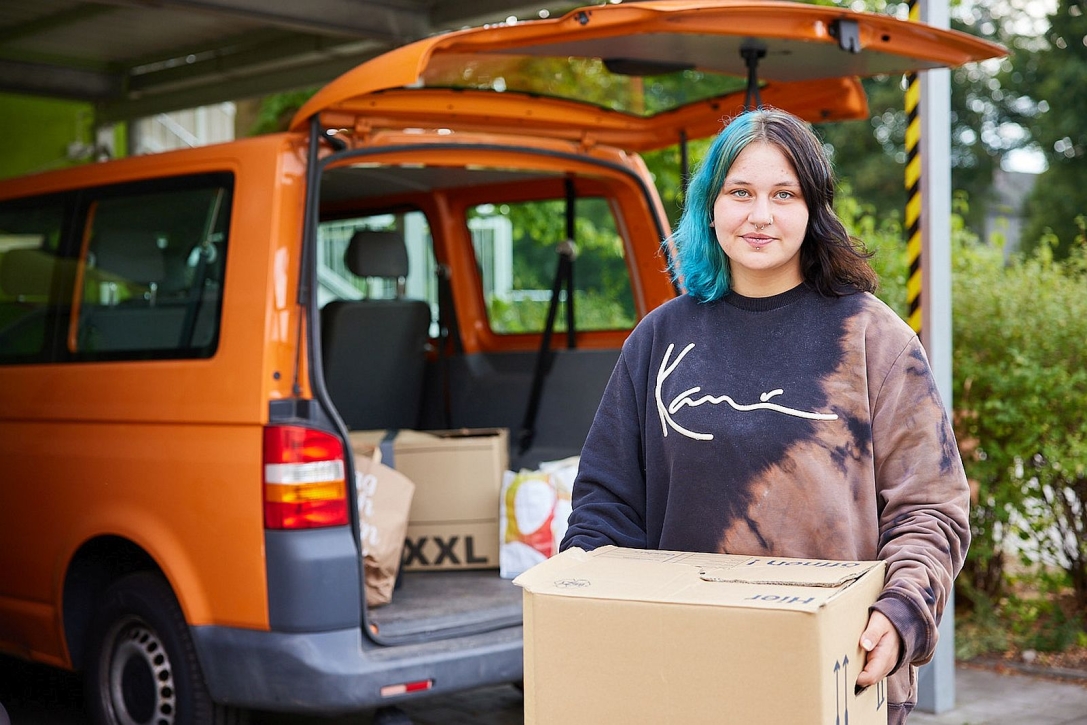 Junge Frau mit Umzugskarton vor Auto